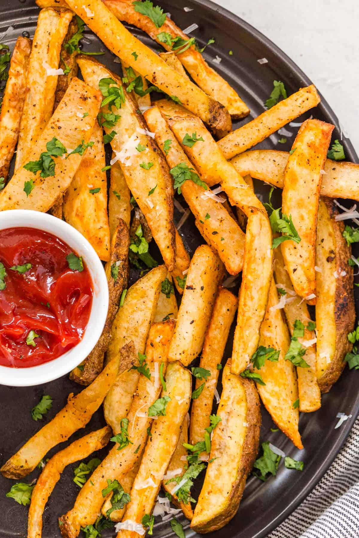 Homemade Air Fryer French Fries on a black plate with parsley garnish and ketchup to dip