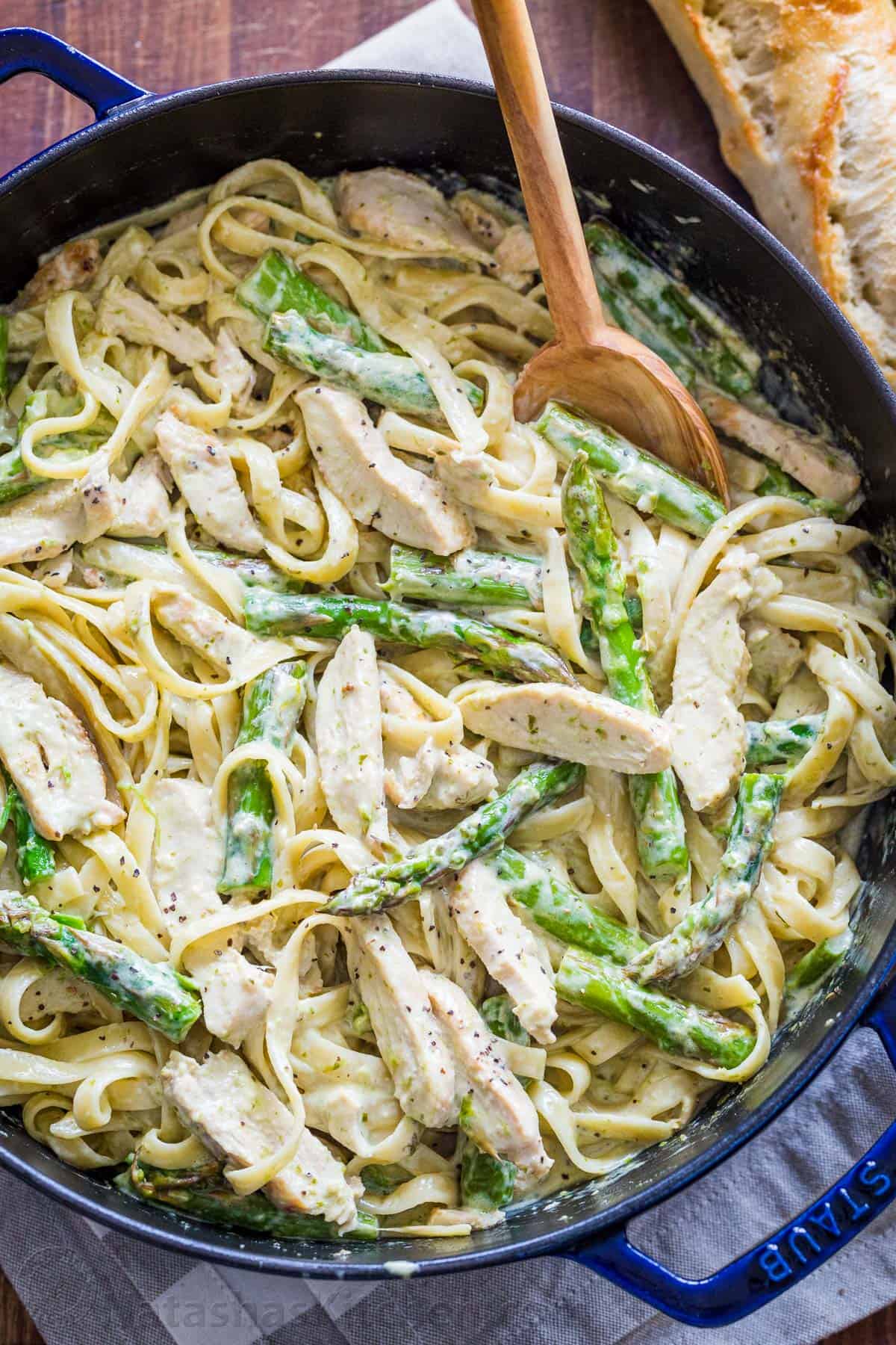 Chicken Pesto pasta in a blue skillet with asparagus and mixing spoon