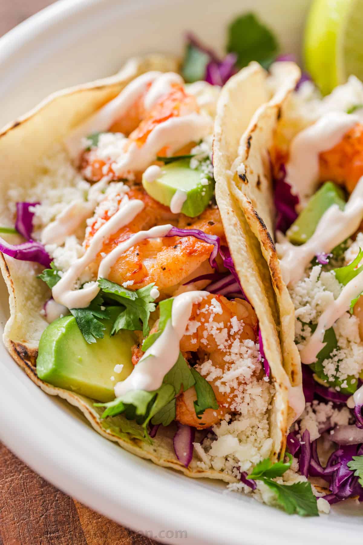 Side profile of tacos laying on platter loaded with shrimp and drizzled with garlic-lime crema sauce